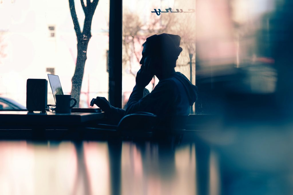 Photo of a guy working on his laptop, in a coffee shop, while talking on the phone.