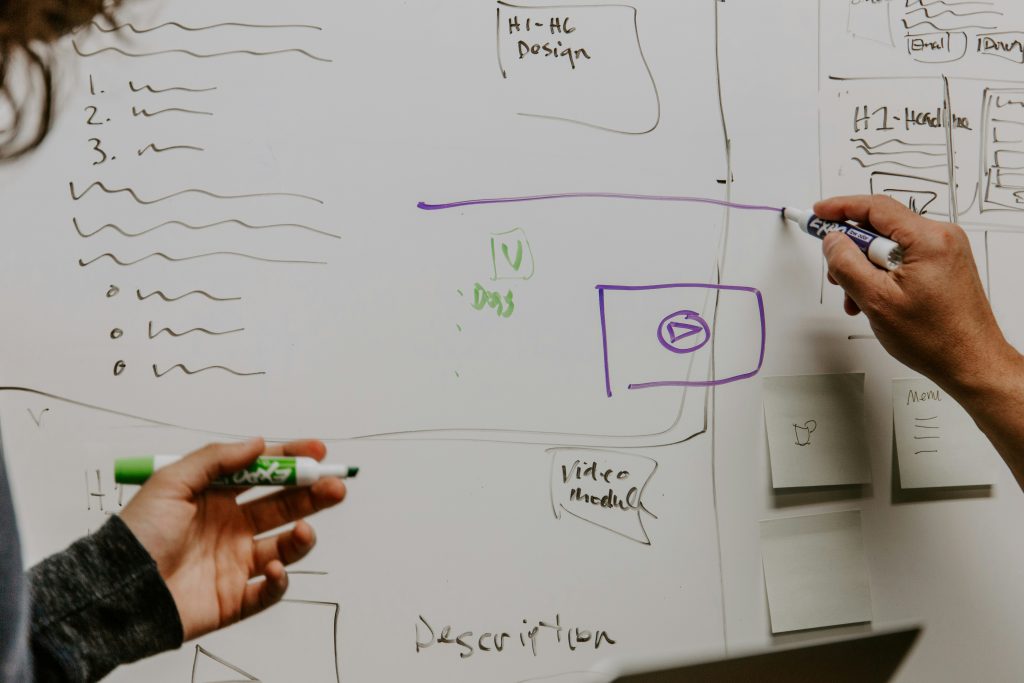 Photo of two people working on a white board, brain storming ideas.